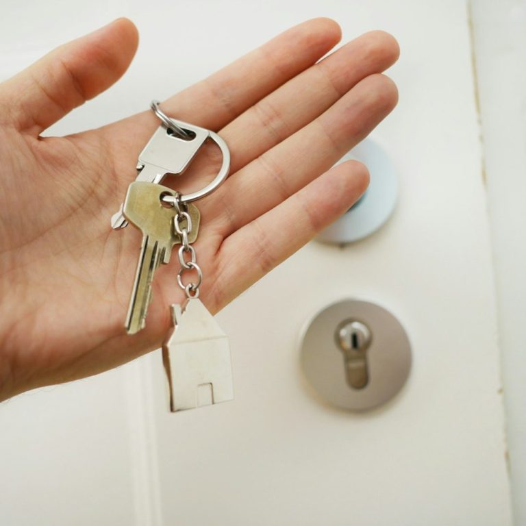 Handing house keys over to freshly prepared home Hand holding keys with a house keychain, positioned near a door lock.